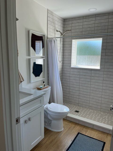 Bathroom with white vanity, toilet, and shower with gray tile and light wood flooring.