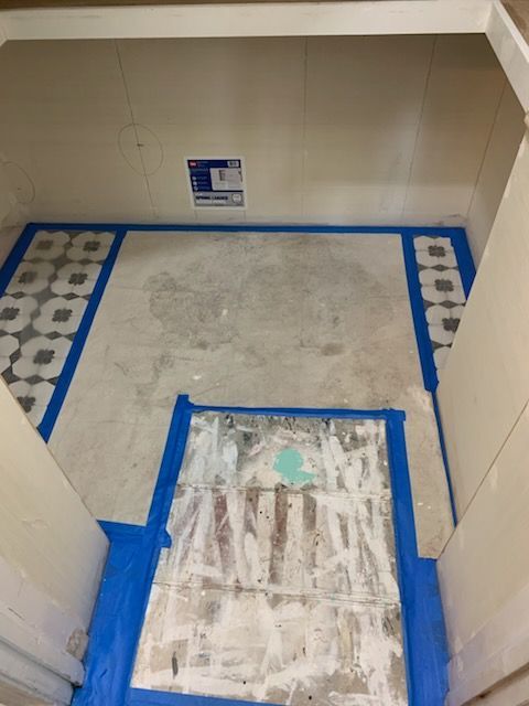 Room with exposed floorboards and tiled borders taped with blue tape, prepared for flooring.
