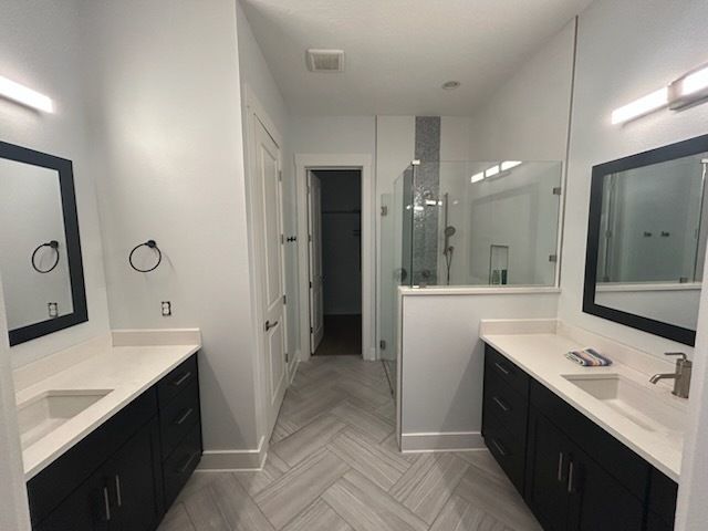 Modern bathroom with two vanities, herringbone floor, and glass shower.