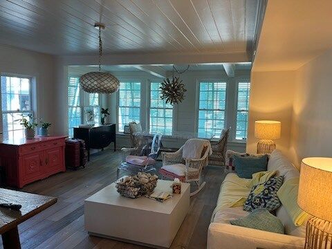 Bright living room with a white sofa, wooden floor, and dining area visible through an opening.