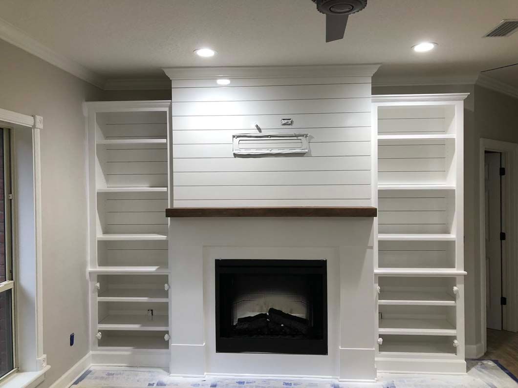 A living room with a fireplace , shelves and a ceiling fan.