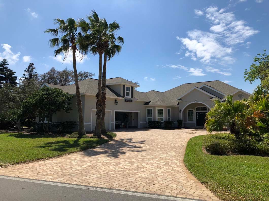 A large house with a driveway and palm trees in front of it.