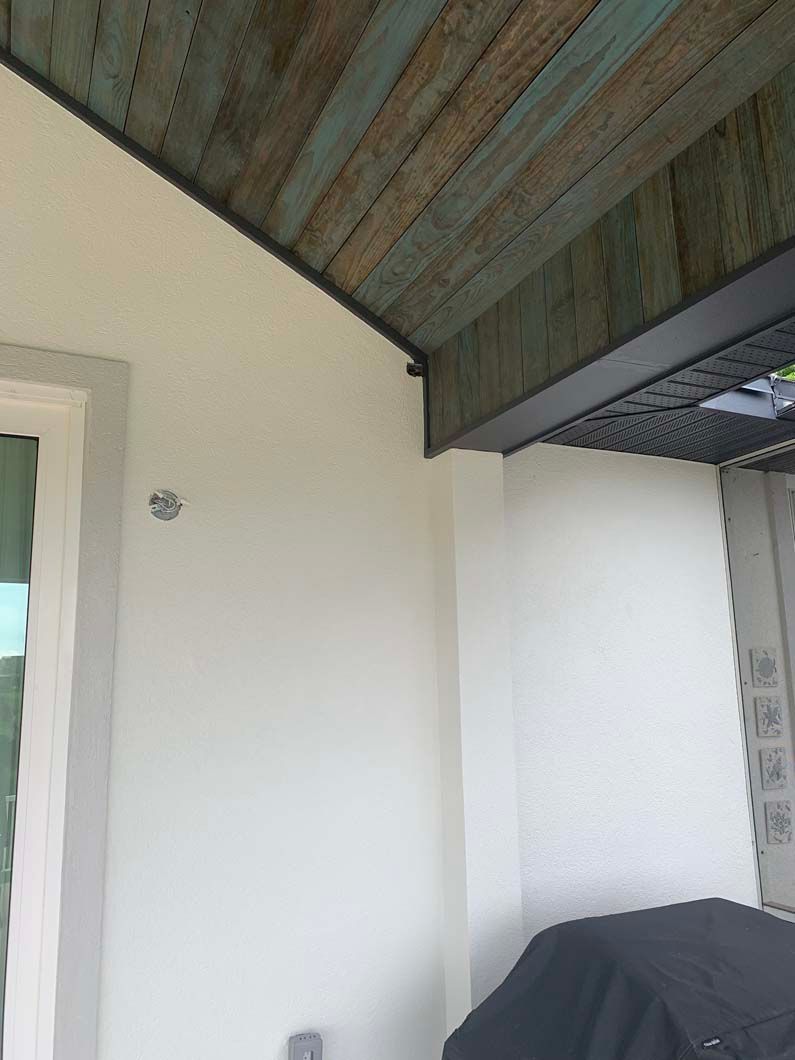 A white wall with a wooden ceiling and a grill on it.