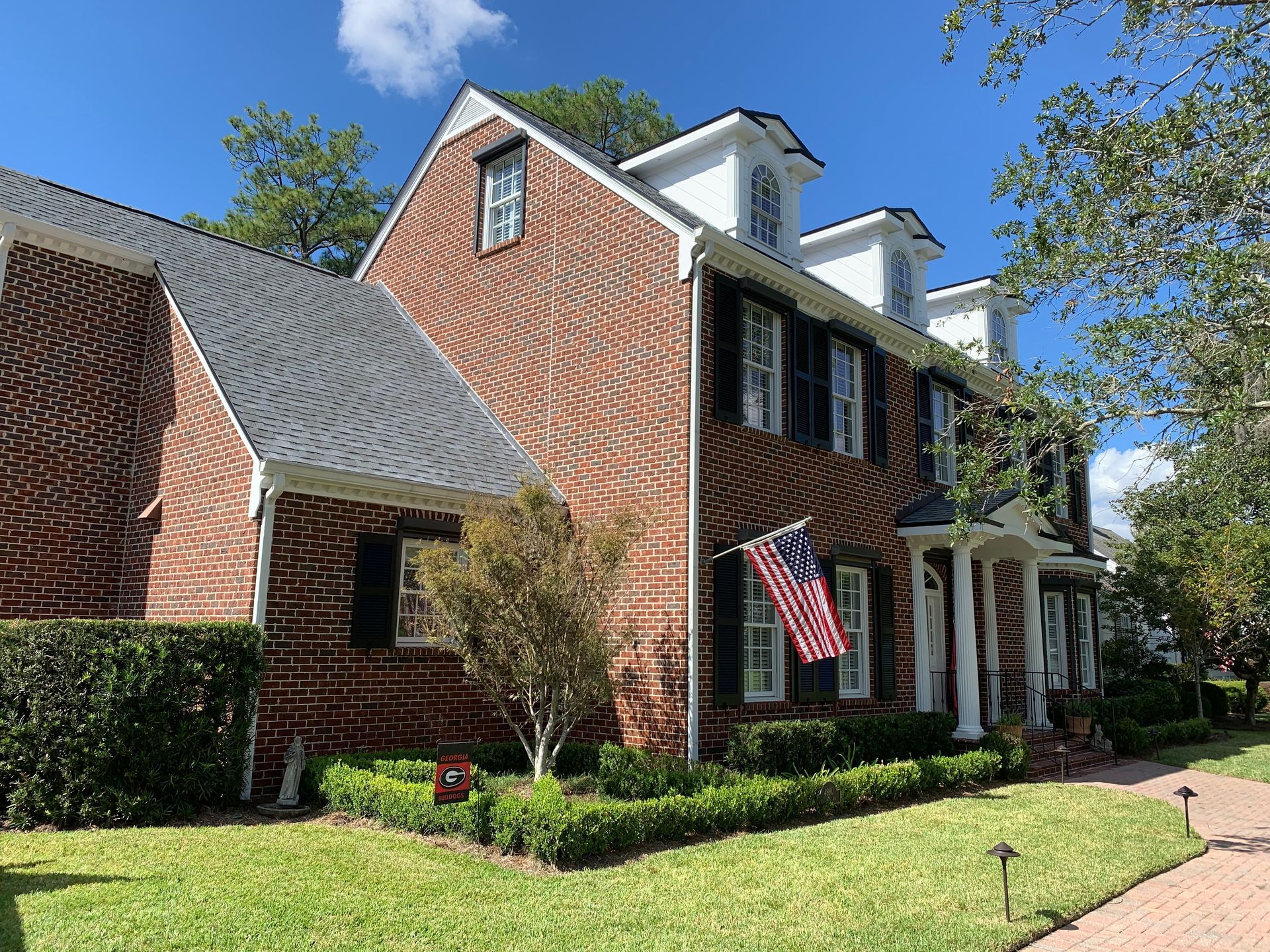 A large brick house with black shutters and an american flag in front of it.