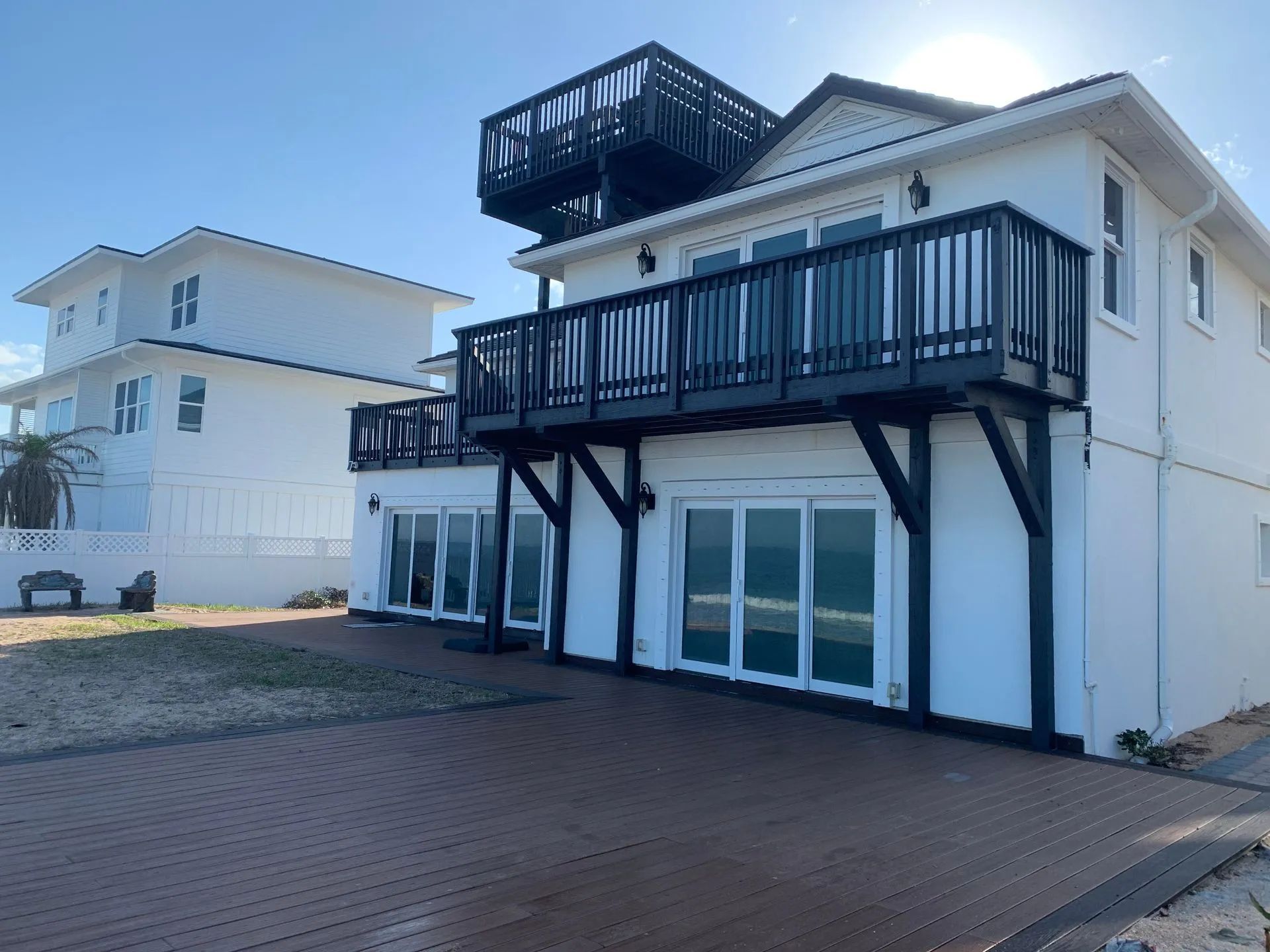 White beachfront house with black balconies, large windows, and a rooftop deck.