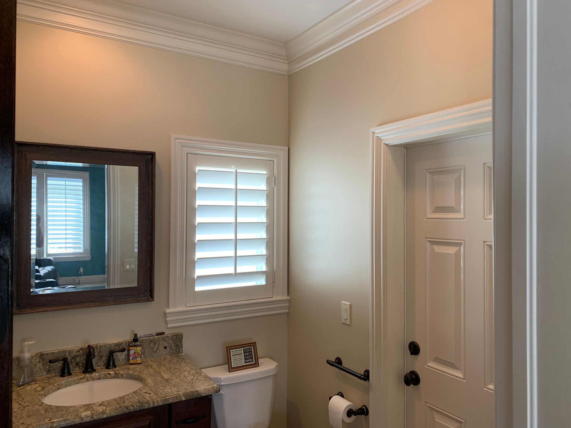 A bathroom with a sink , toilet , mirror and shutters.