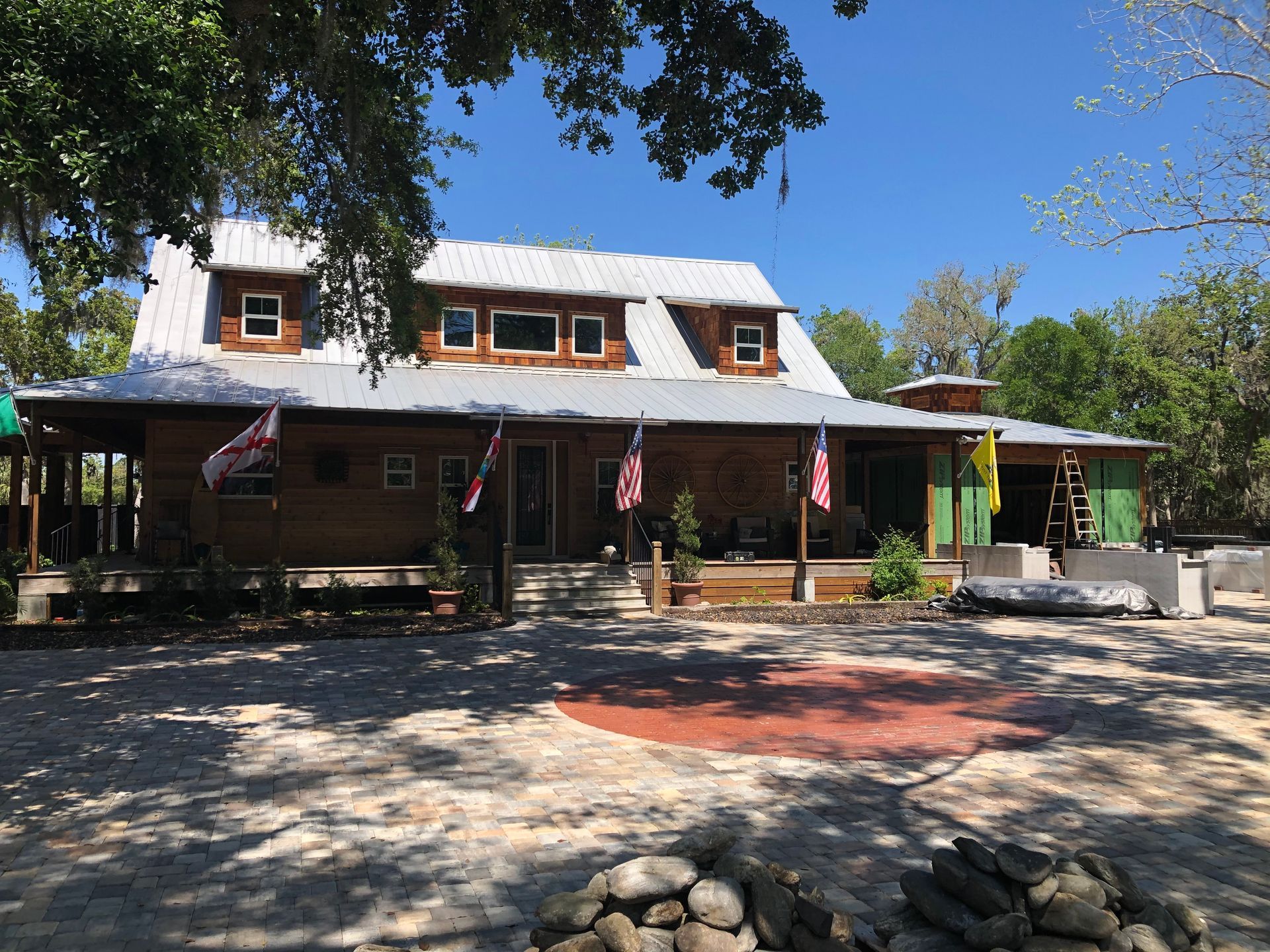 A large wooden house with a metal roof is surrounded by trees and rocks.
