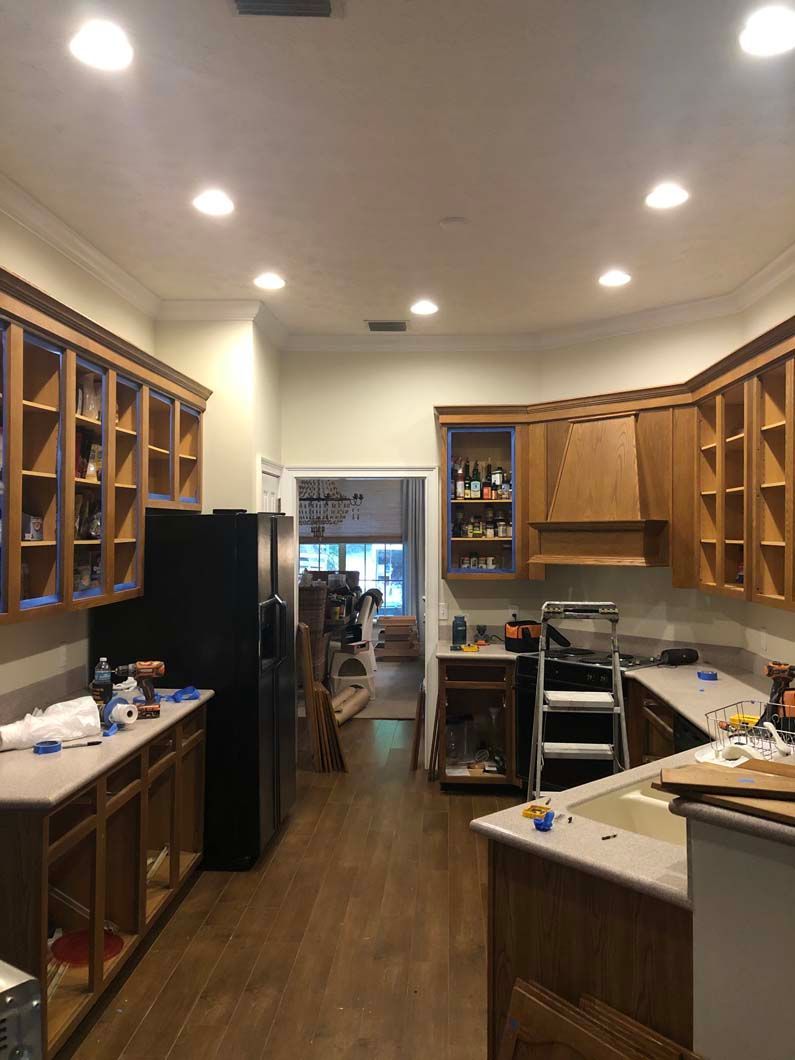A kitchen is being remodeled with wooden cabinets and a black refrigerator.