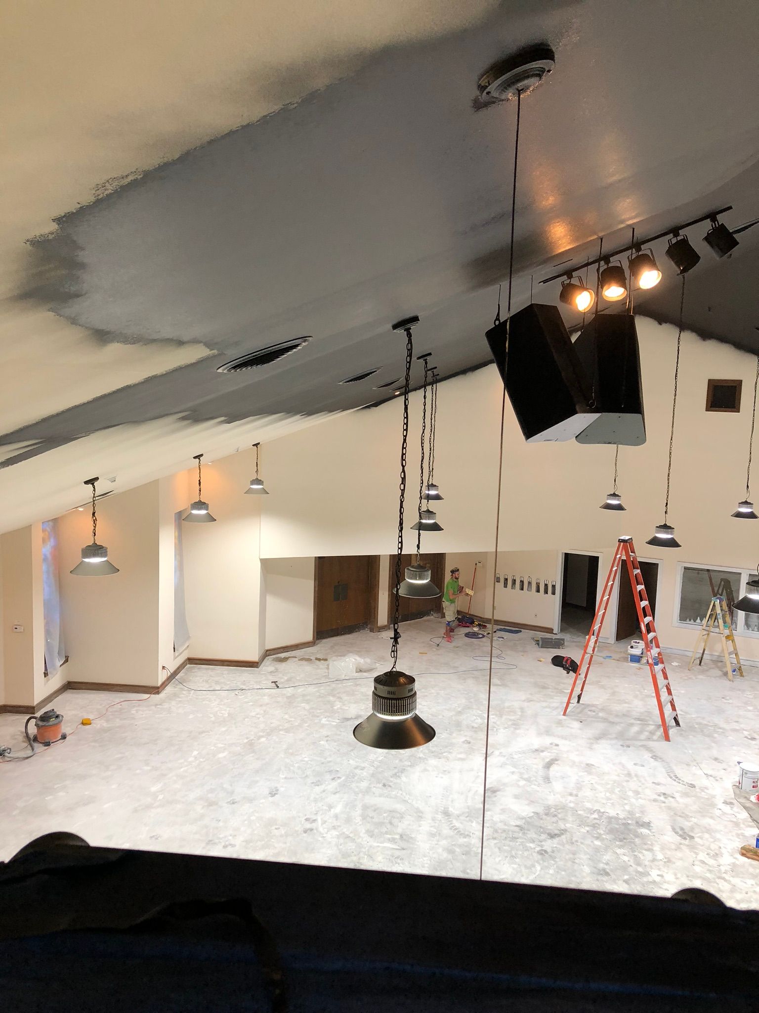 Construction site: interior view with exposed ceiling, gray paint, pendant lights, speakers, and construction materials.