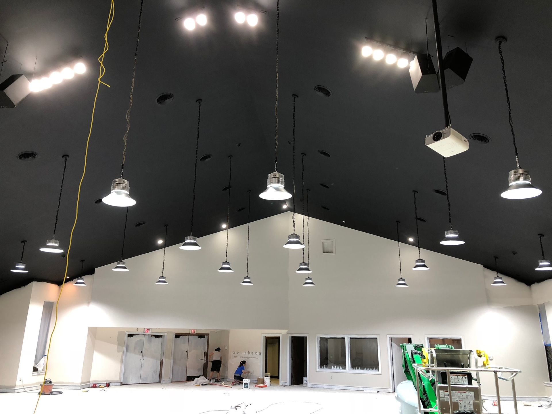 Interior of a newly constructed room with black ceiling, white walls, and hanging lights. Construction workers are visible.