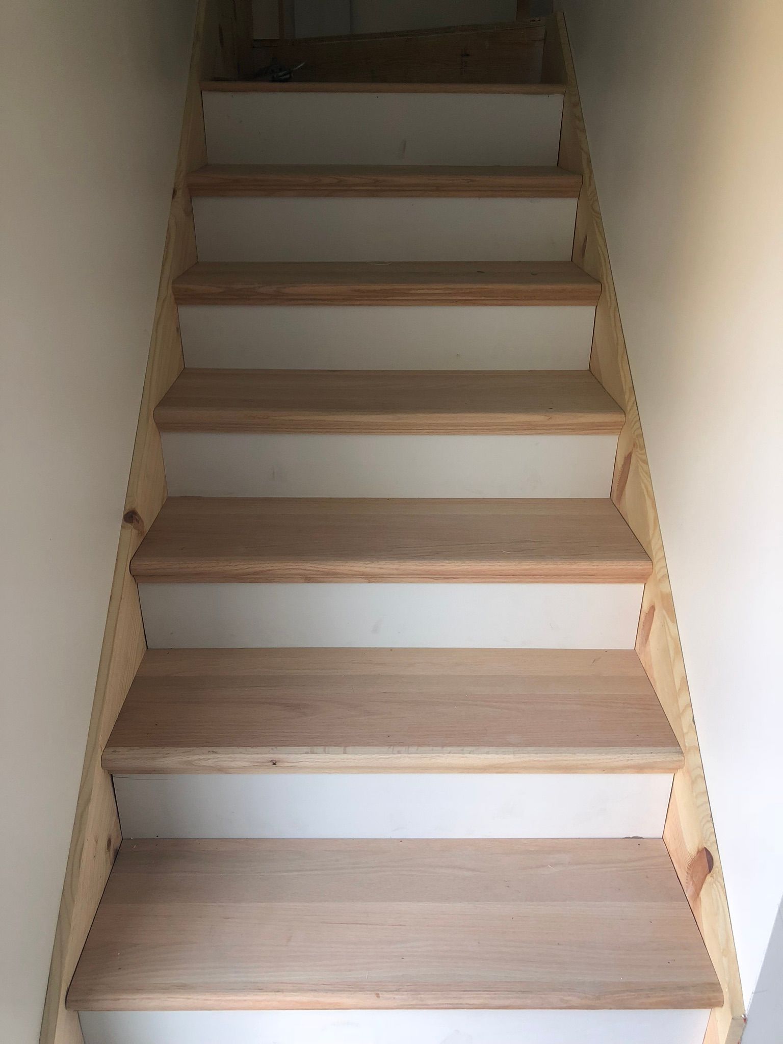 Staircase with wooden steps and white risers, leading upwards between white walls.