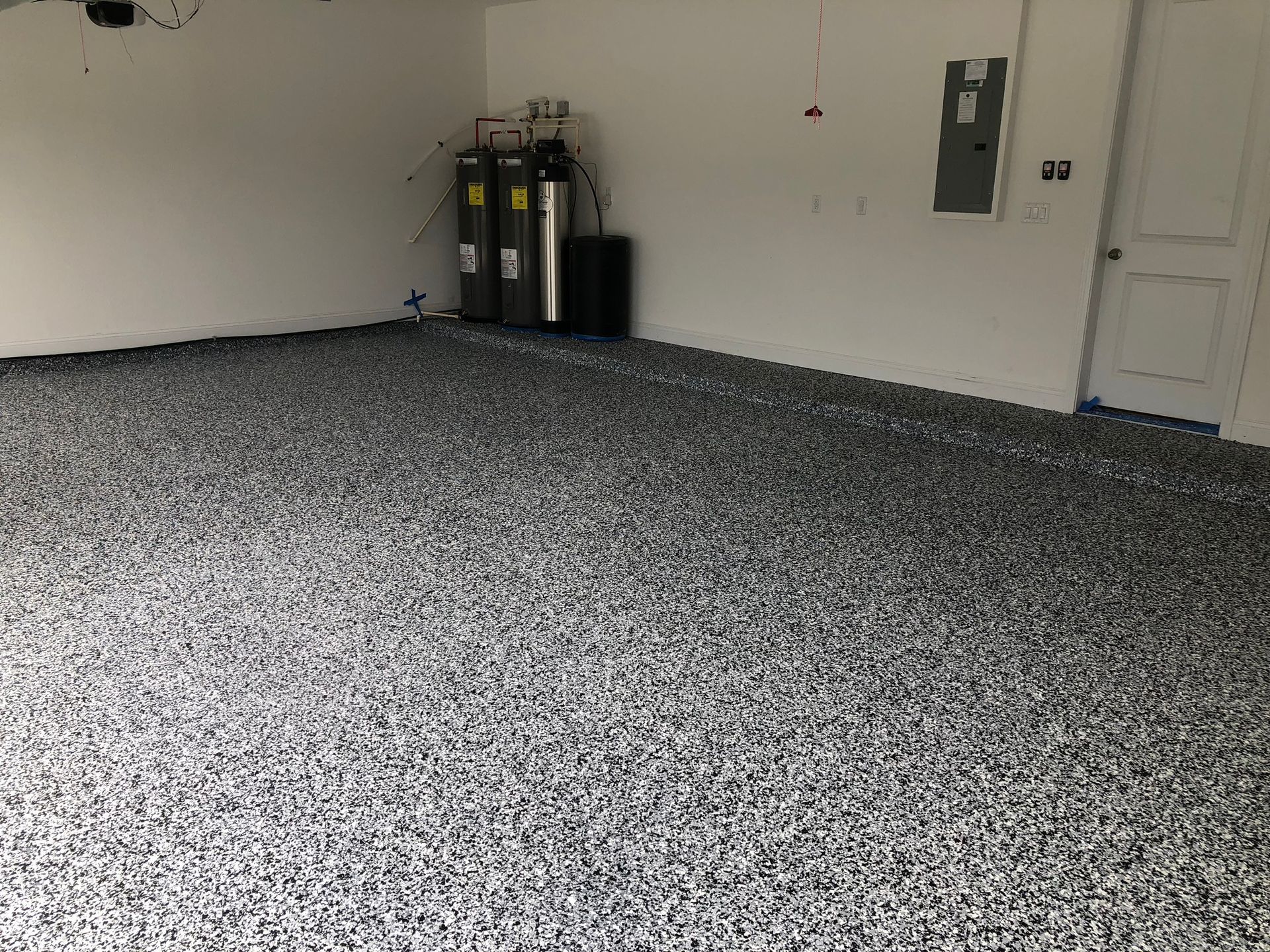 Garage with a speckled, dark-gray epoxy floor; water filtration system, electrical panel, and a door visible.