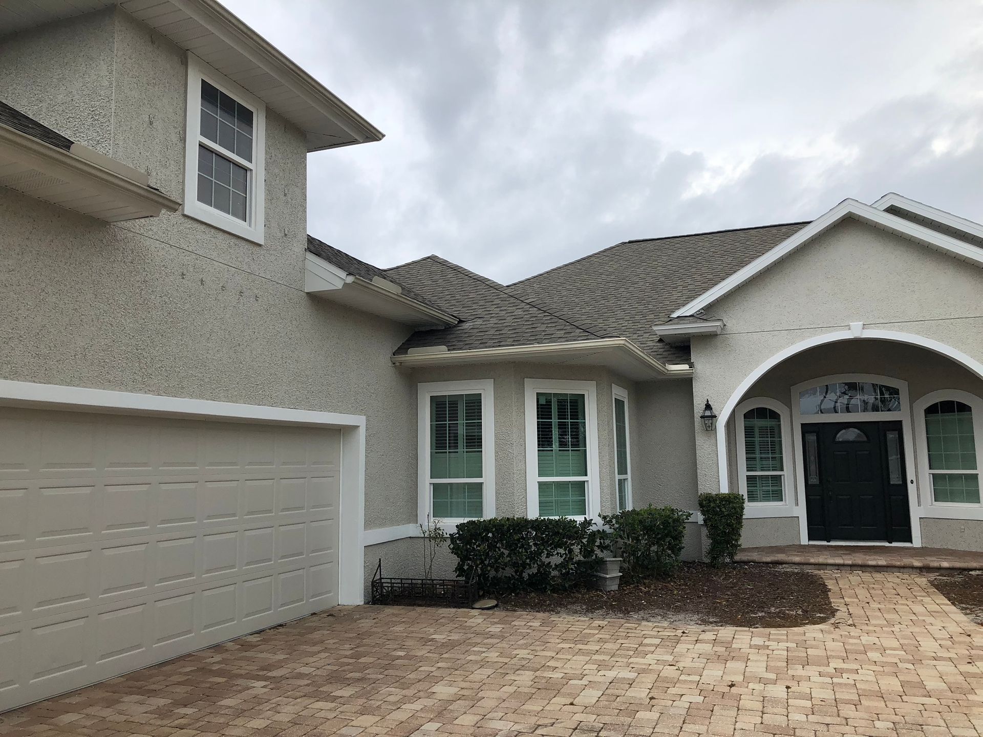 Tan stucco house with arched doorway, windows, and garage. A brick walkway leads to the front door.
