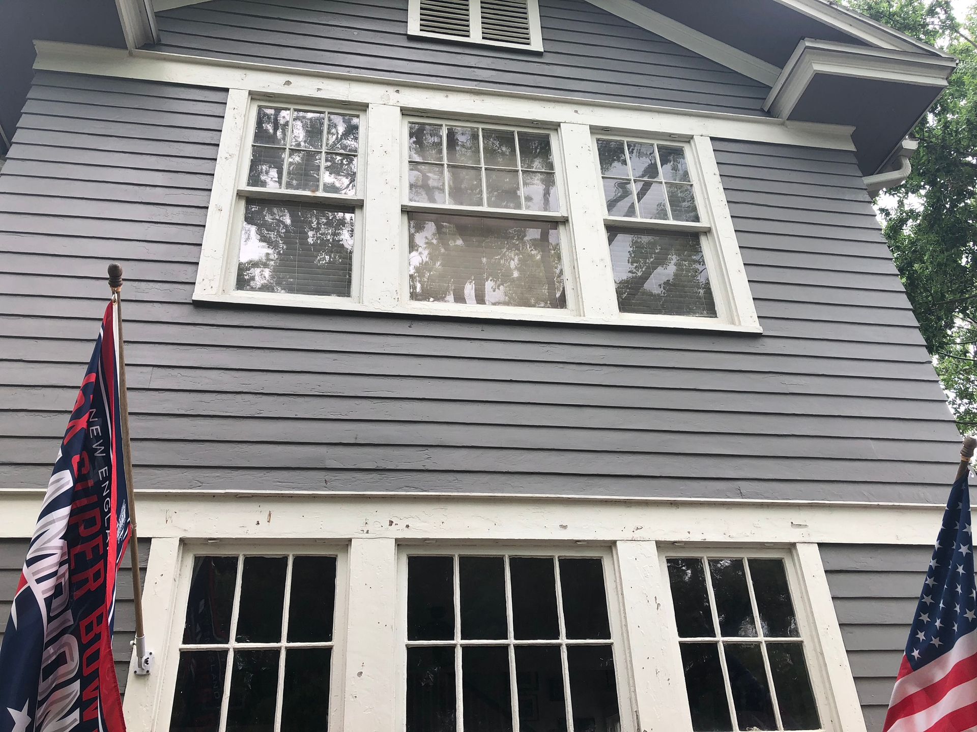 Gray house with white-trimmed windows; flags in foreground.