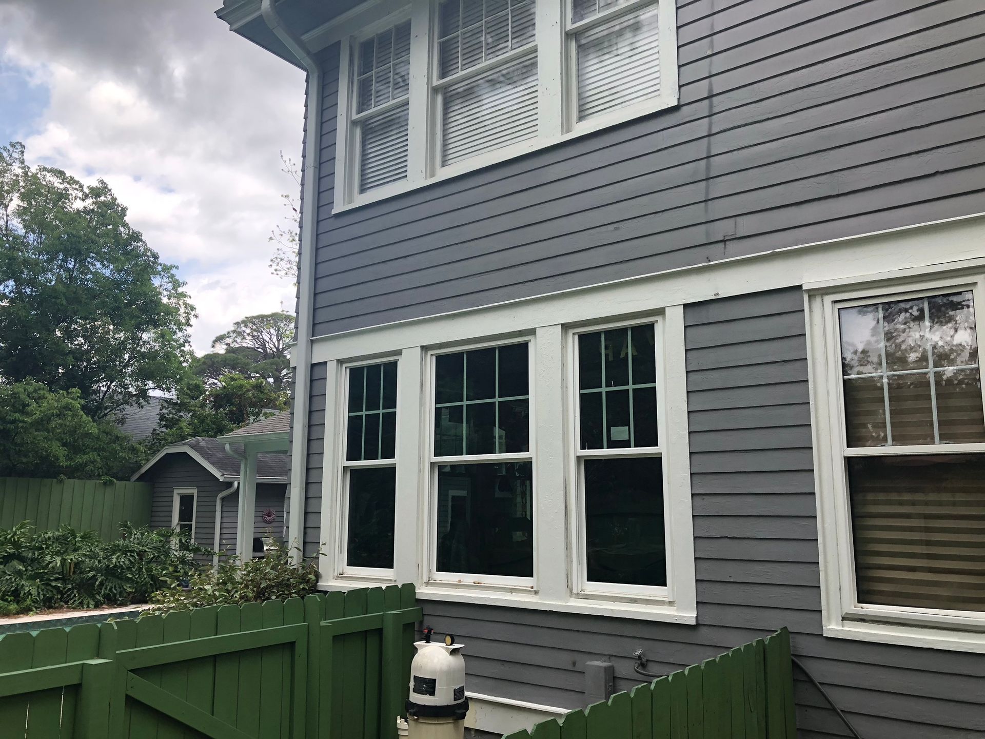 Gray house siding with white trim, windows, and a green fence.