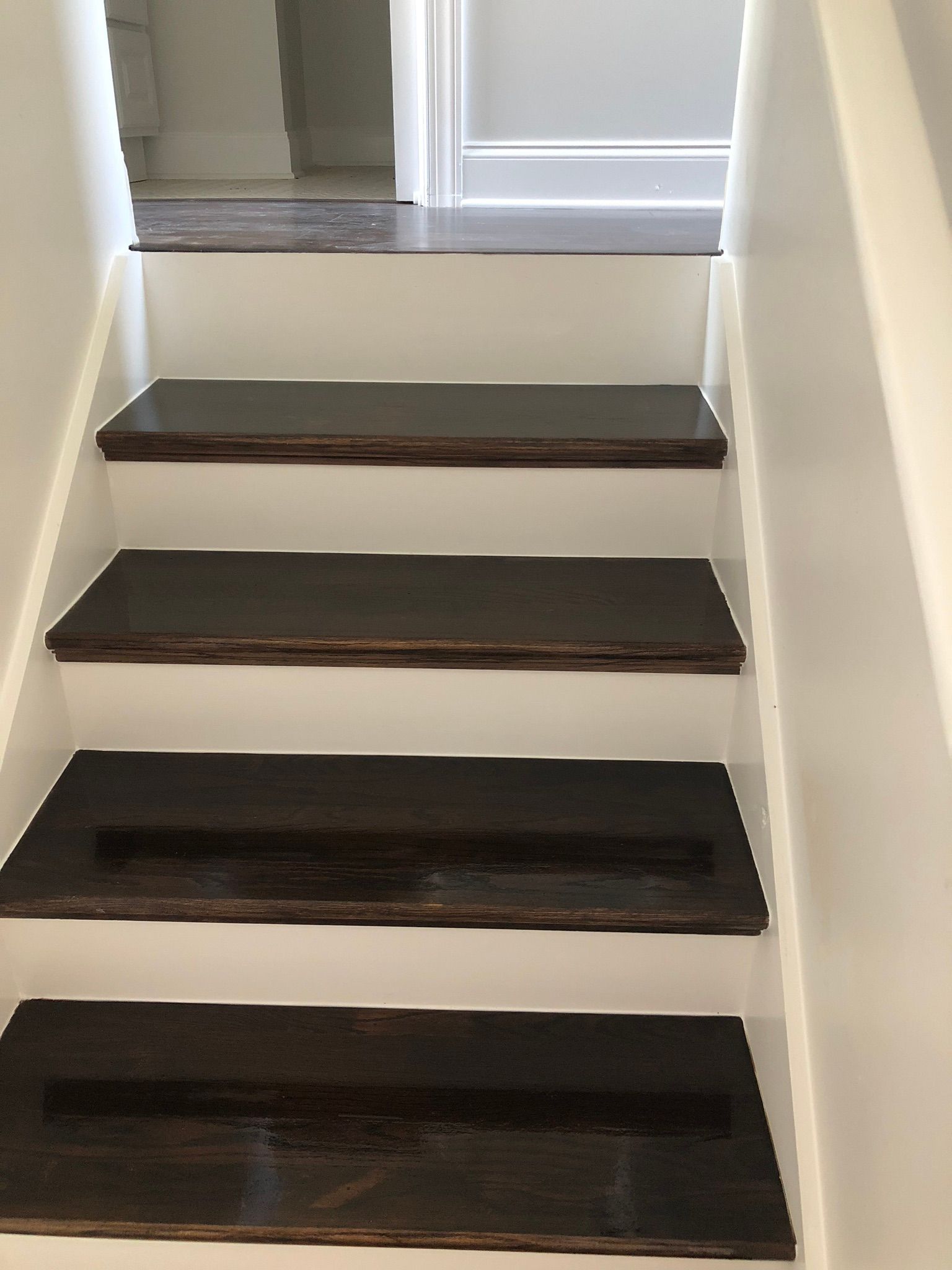 Staircase with dark brown treads and white risers, ascending toward a doorway.