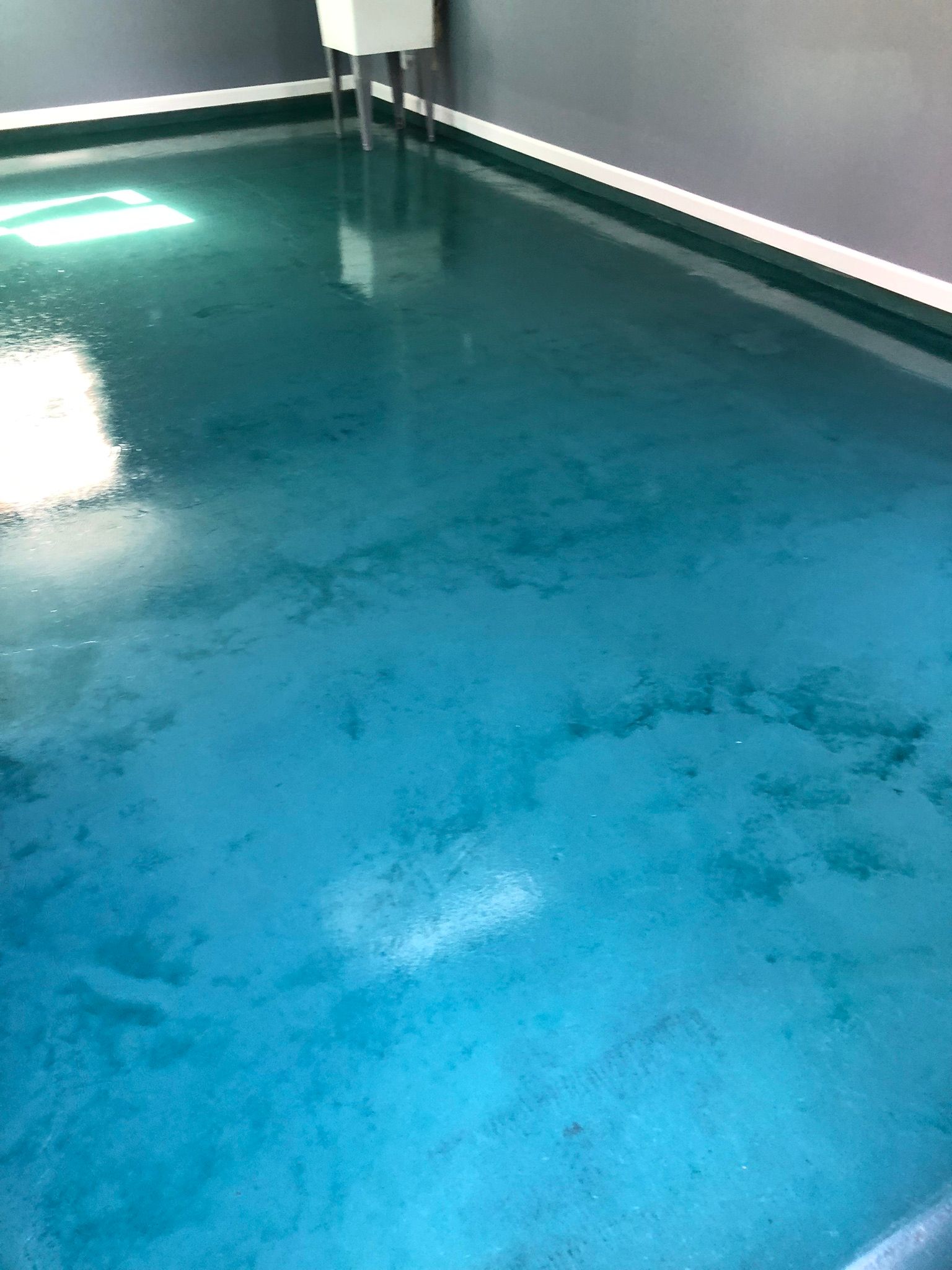 Blue epoxy floor with variations and reflections. White trim along the walls and a white sink in the corner.