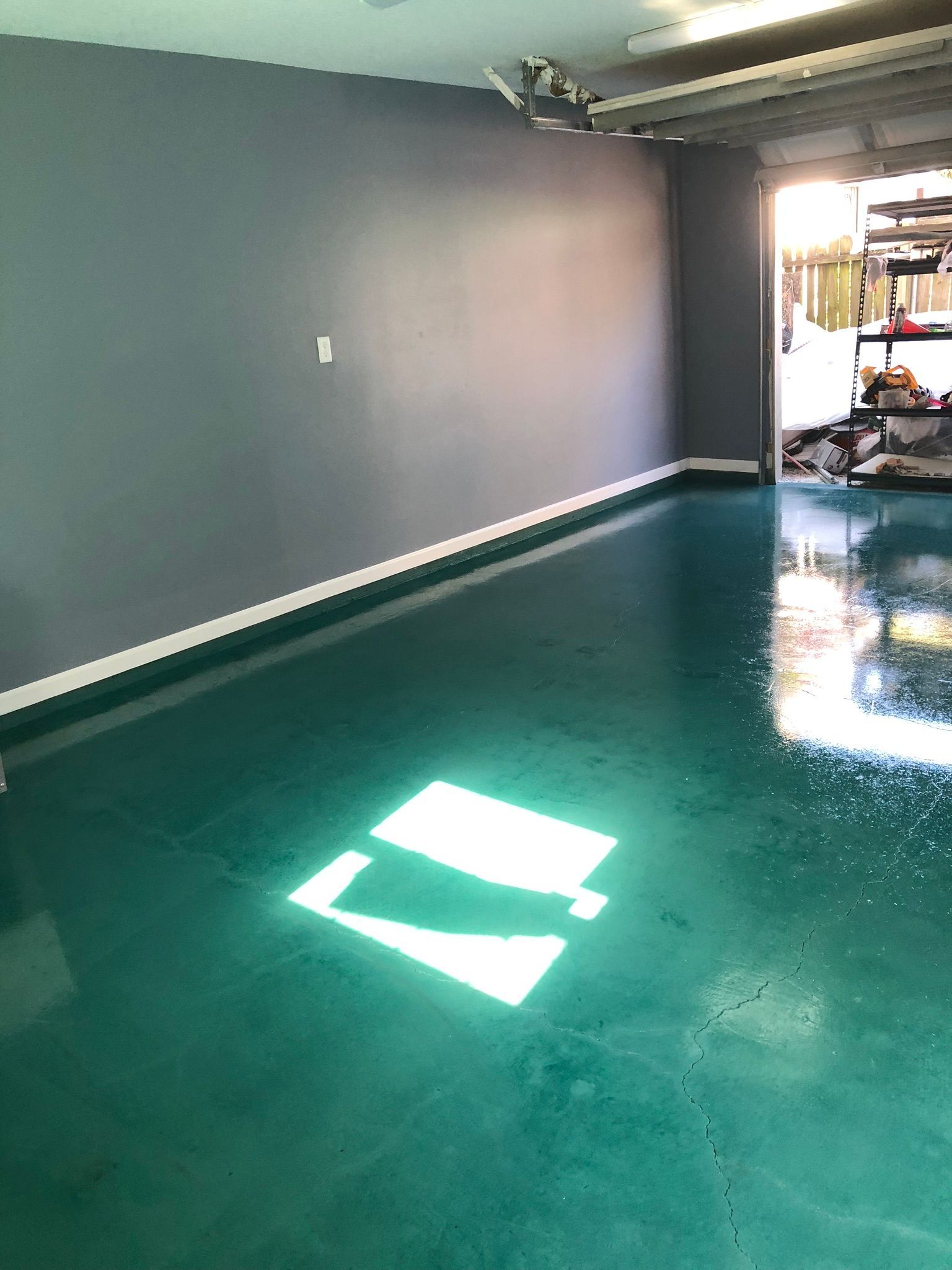 A garage interior with a teal-colored floor and gray walls, the garage door is open.
