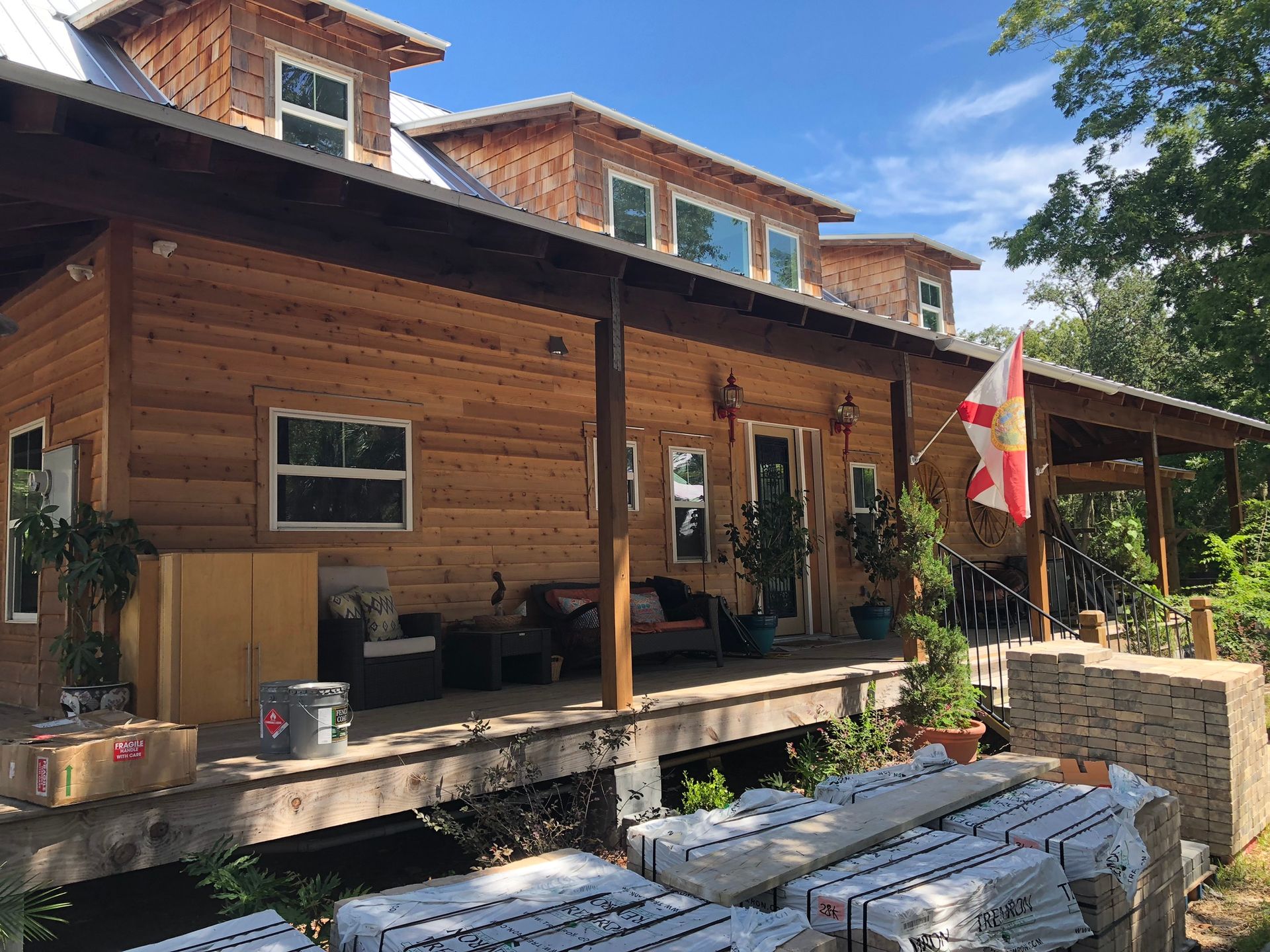 Wooden cabin with a porch, plants, and a Canadian flag on a sunny day.