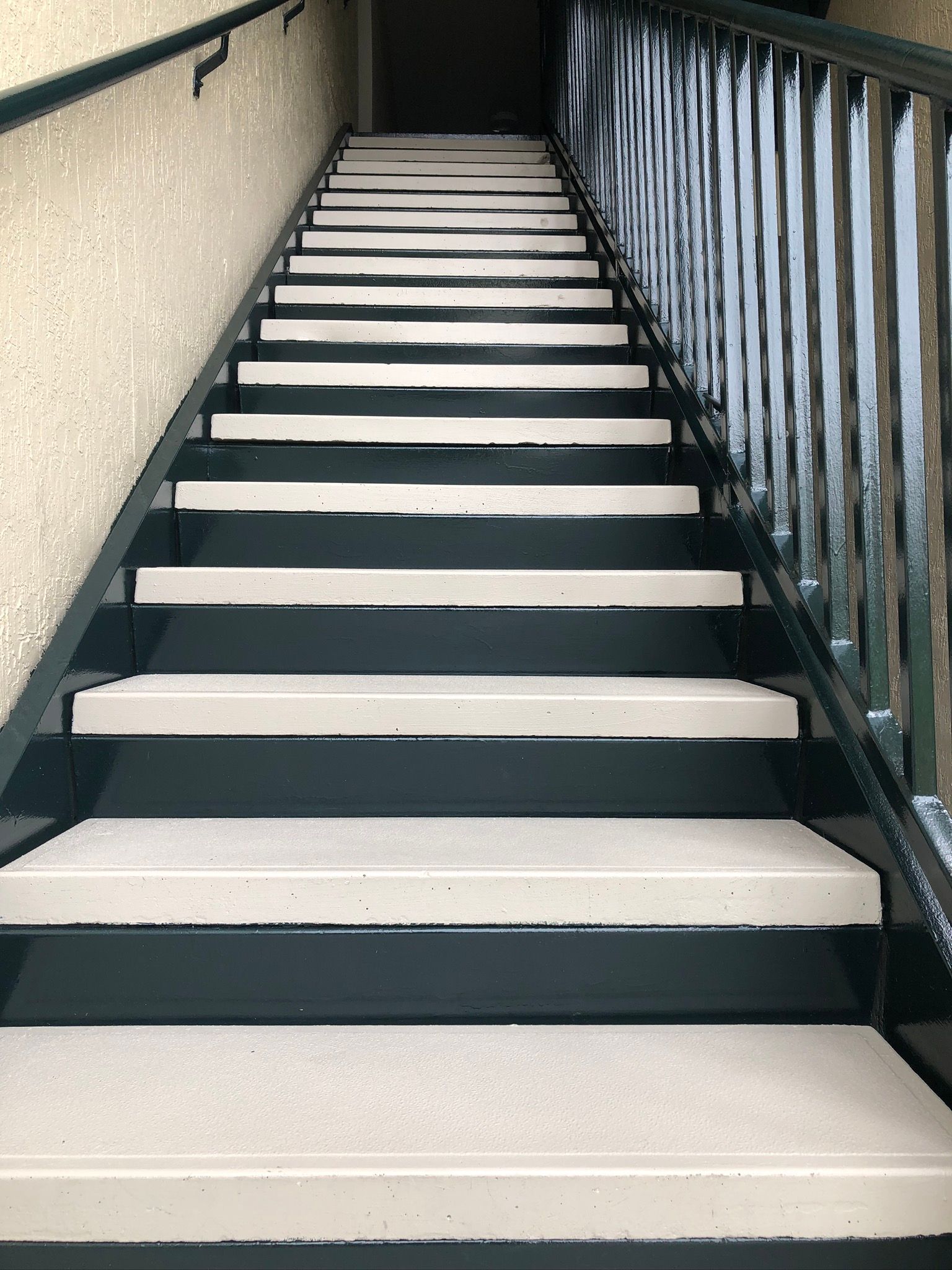 Staircase with white steps, black trim, and green railing.
