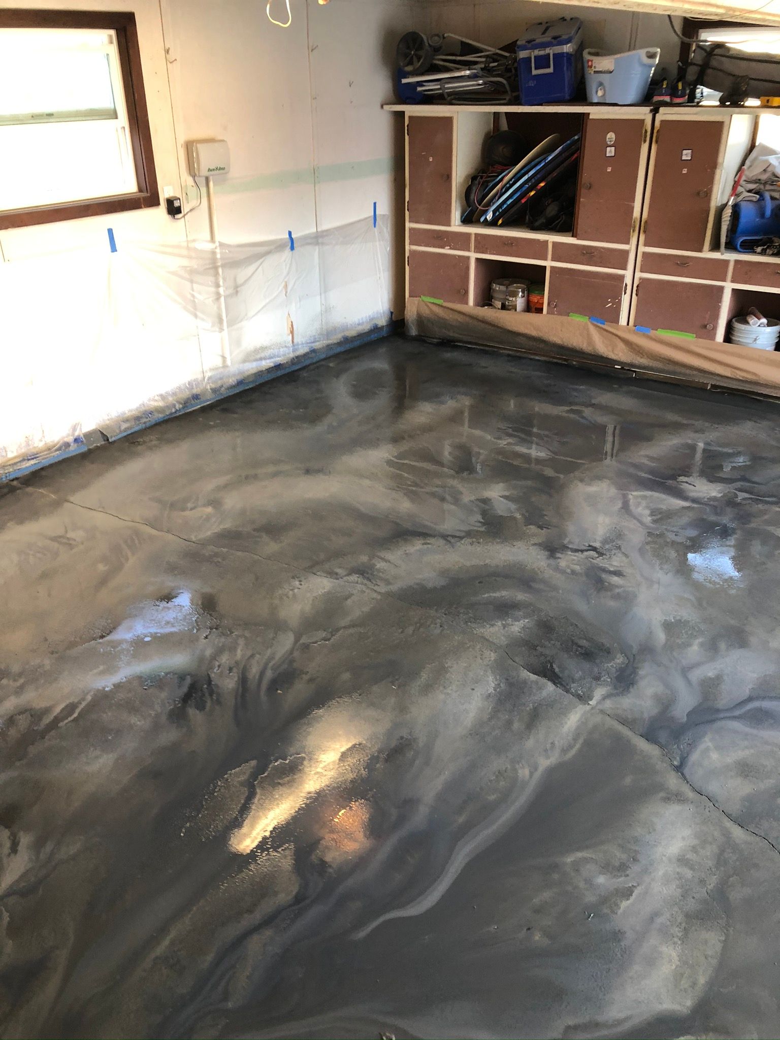 Metallic epoxy garage floor. Silver, gray, and black swirls. Cabinets and a window are in the background.