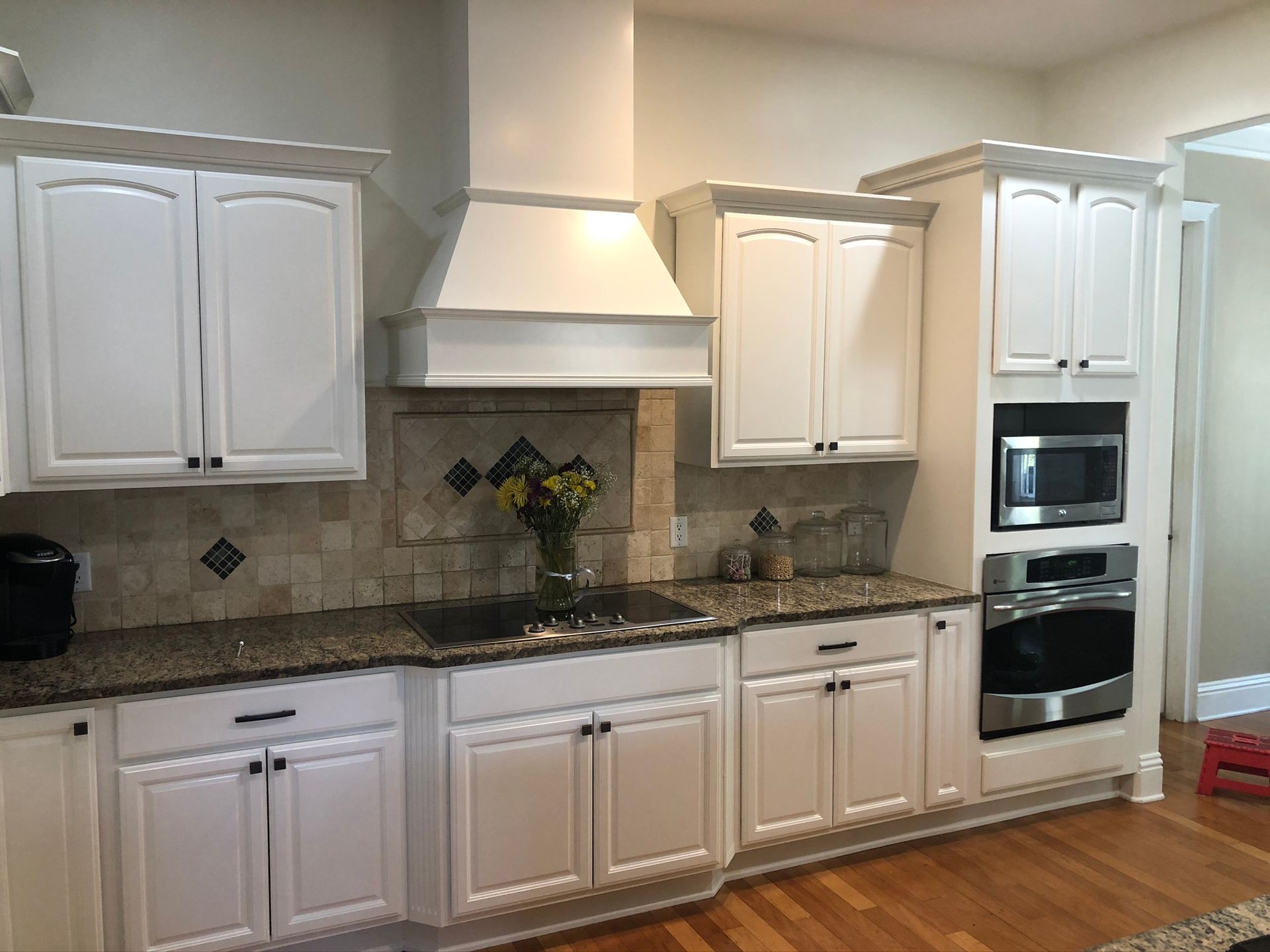 White kitchen cabinets with black countertops, stove, oven, and backsplash with a flower arrangement.