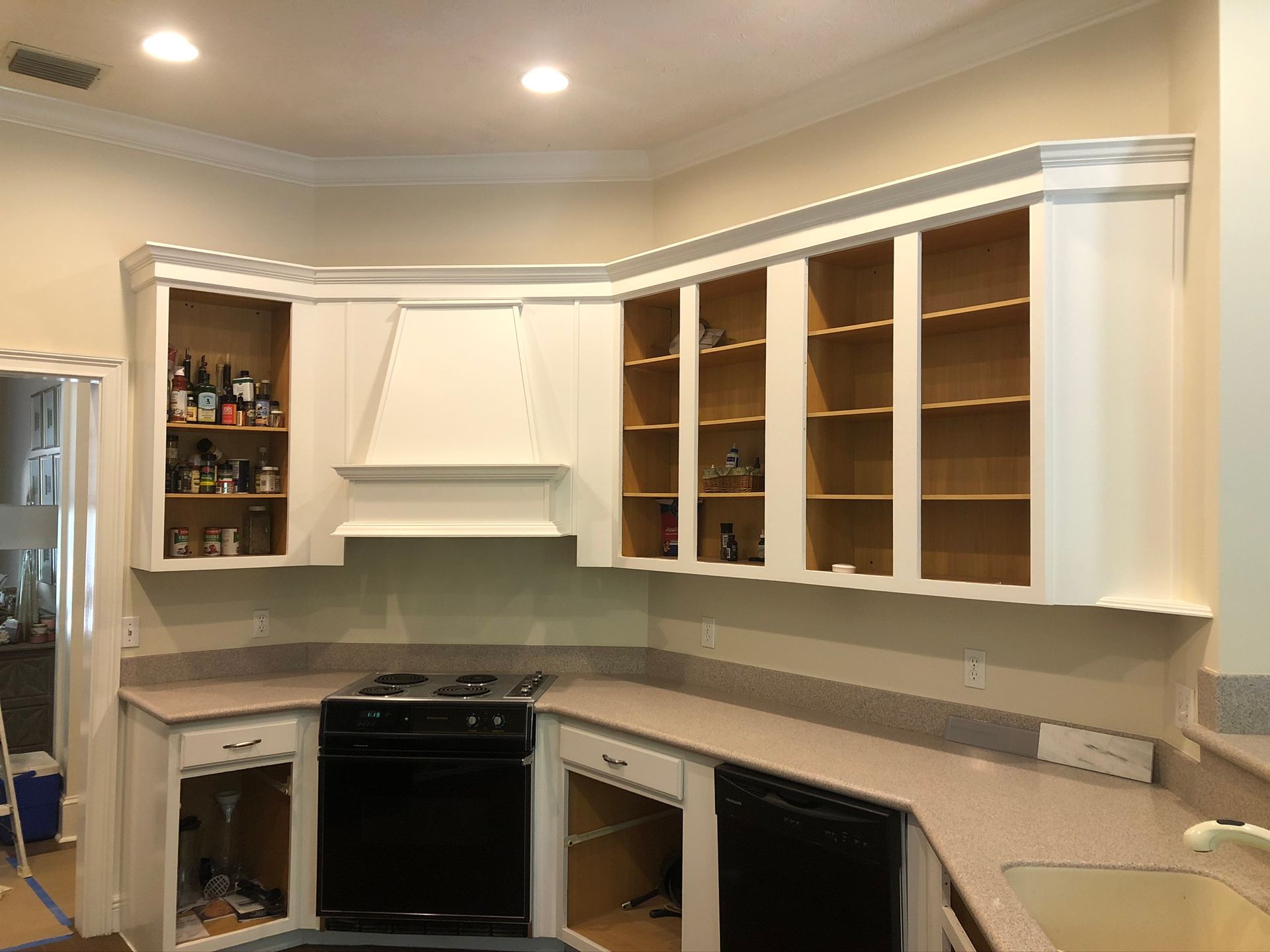 Kitchen cabinets, mostly white, are being installed with some open, cabinets over the stove.