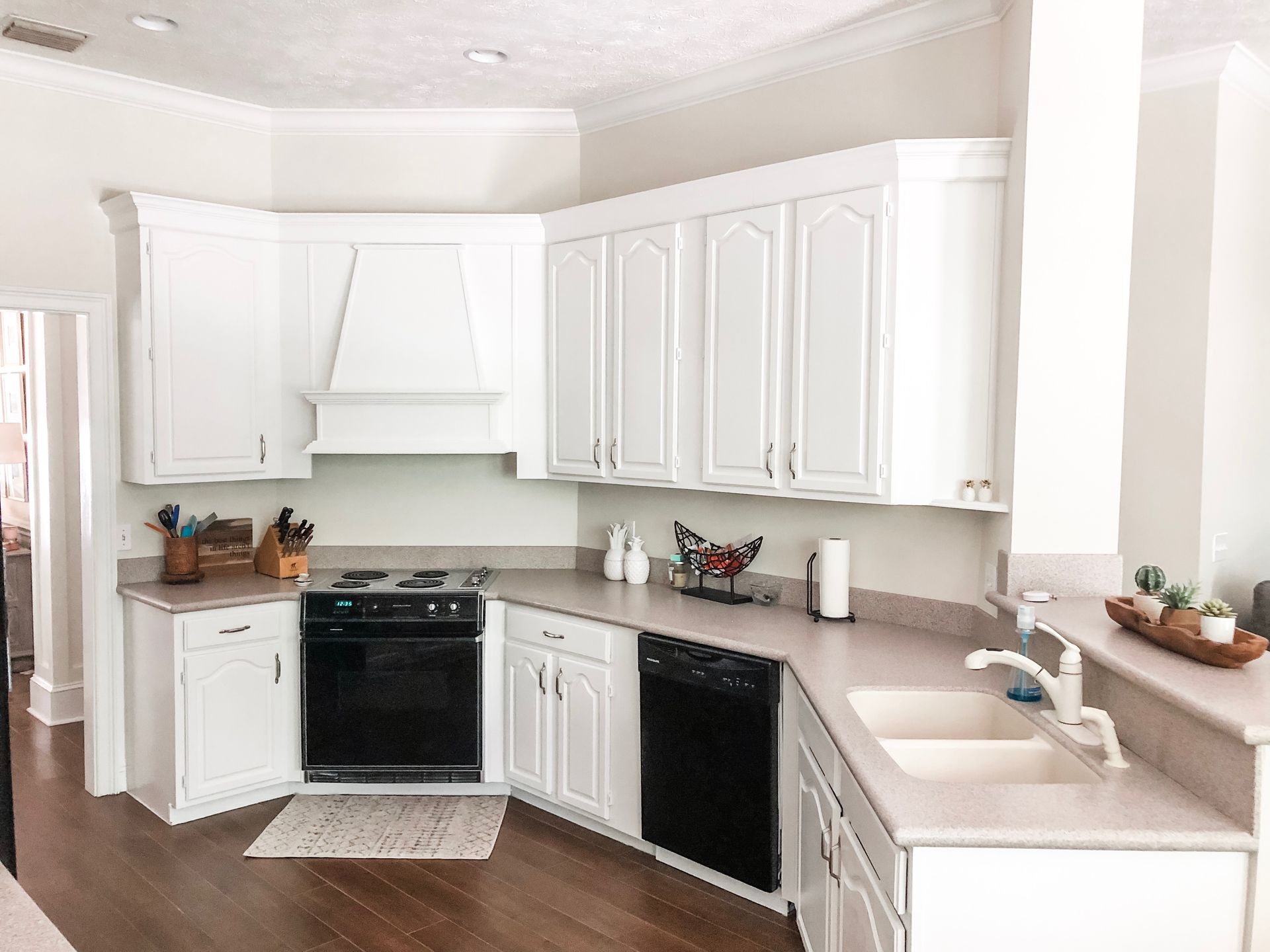 White kitchen with black appliances, light countertops, and wooden floor.