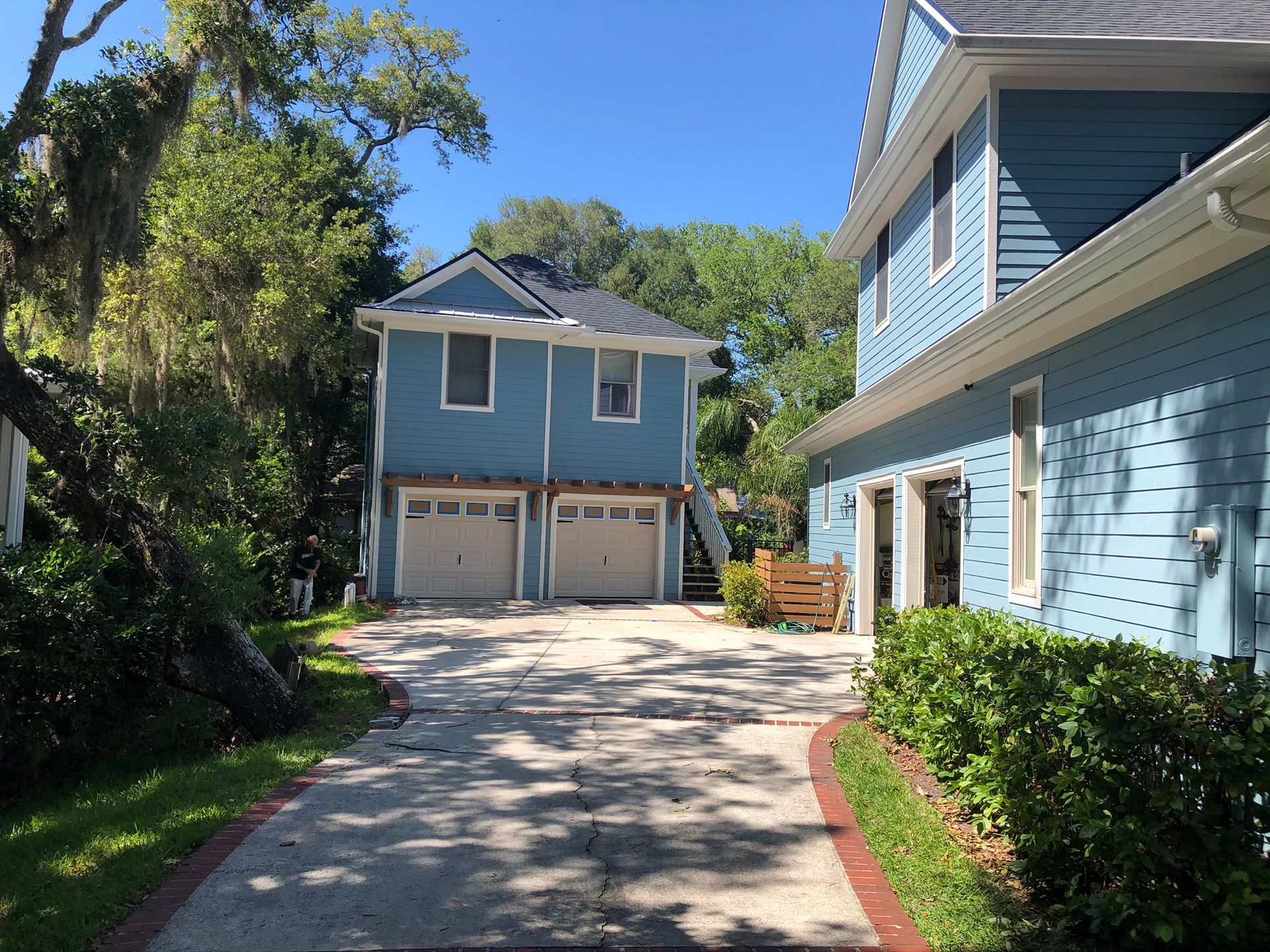 Driveway leading to a two-story blue building with two garage doors, sunny day.