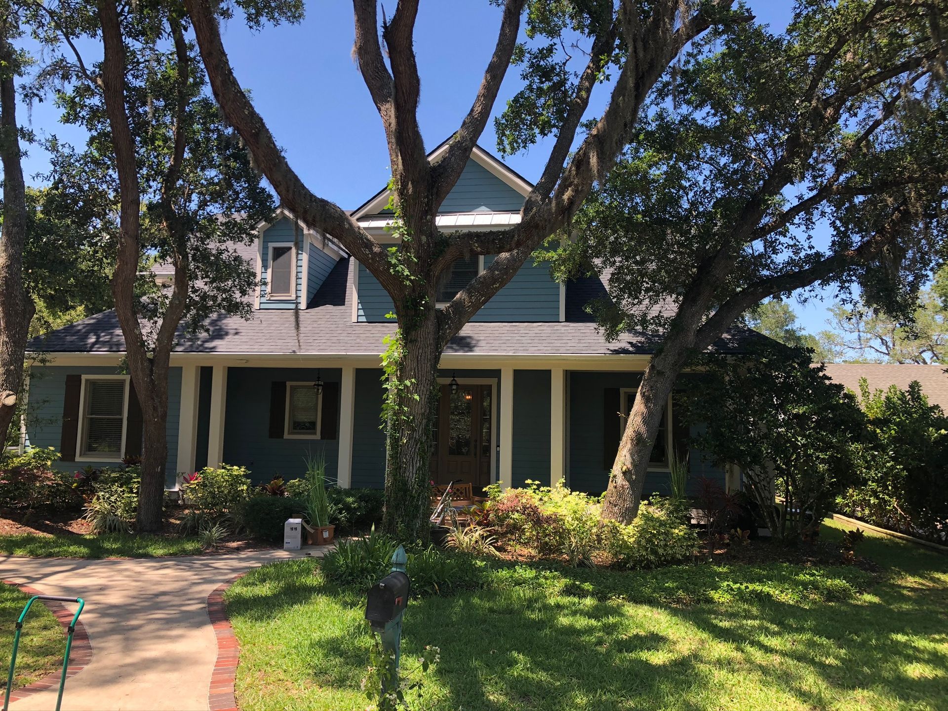 Blue house with porch, surrounded by trees and lawn, under a clear sky.