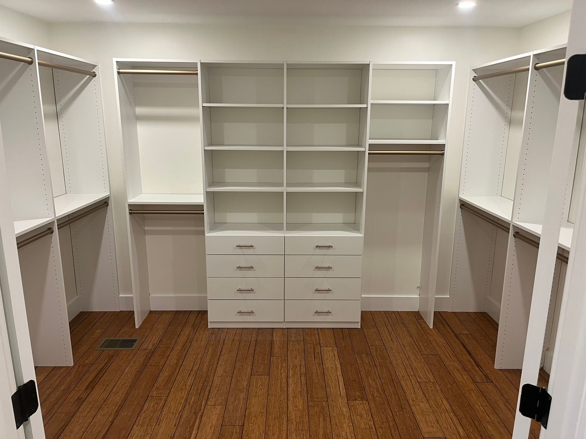 A walk in closet with white shelves and drawers and a wooden floor.