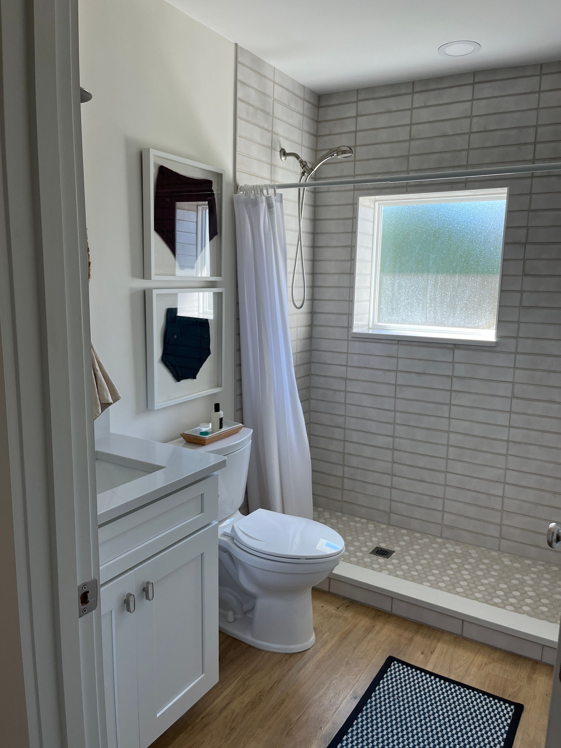 Small bathroom with white vanity, toilet, and shower. Subway tile and a frosted window are visible.