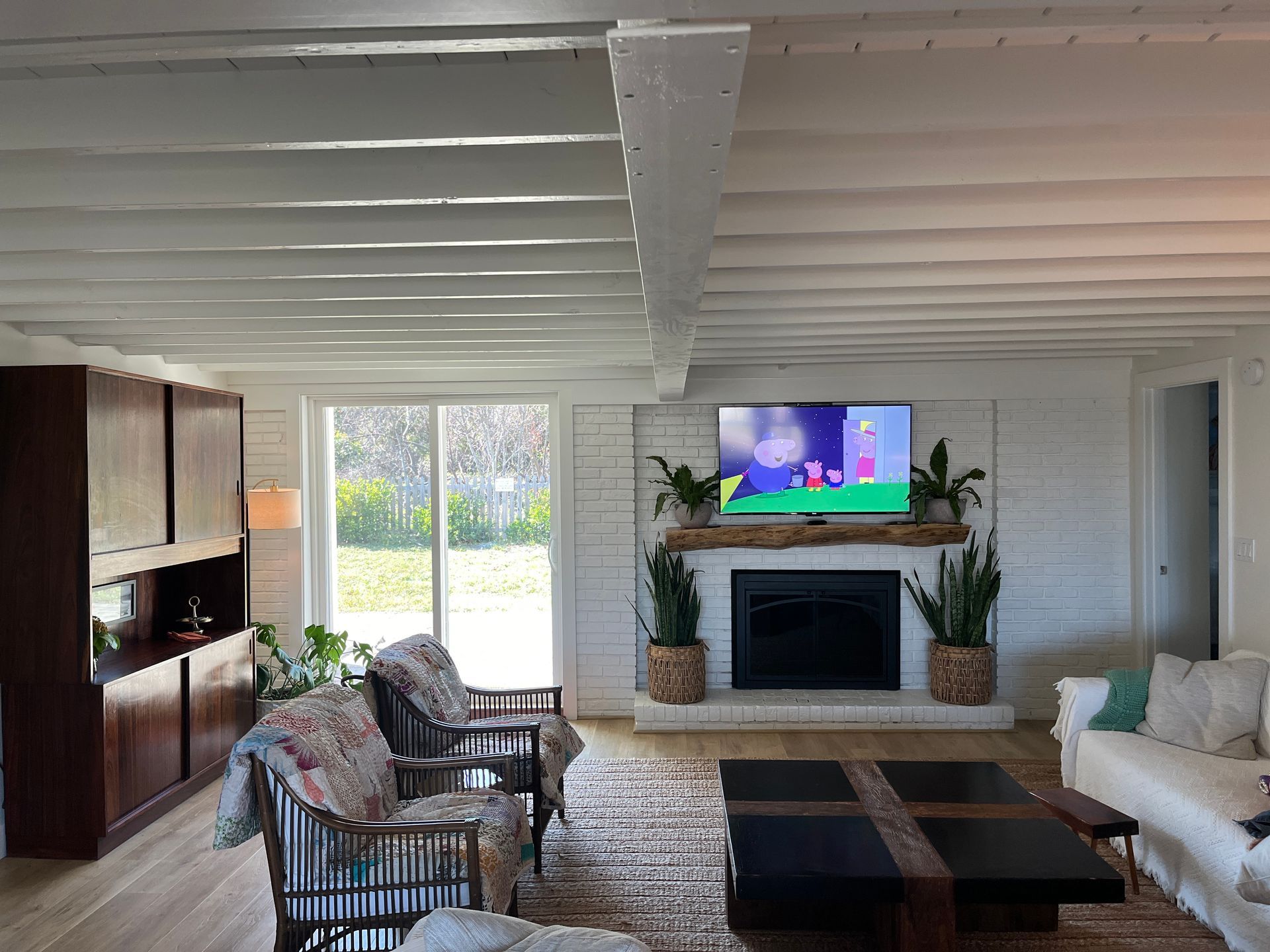 Living room with white brick, fireplace, TV, seating, wood beams, and large cabinets.