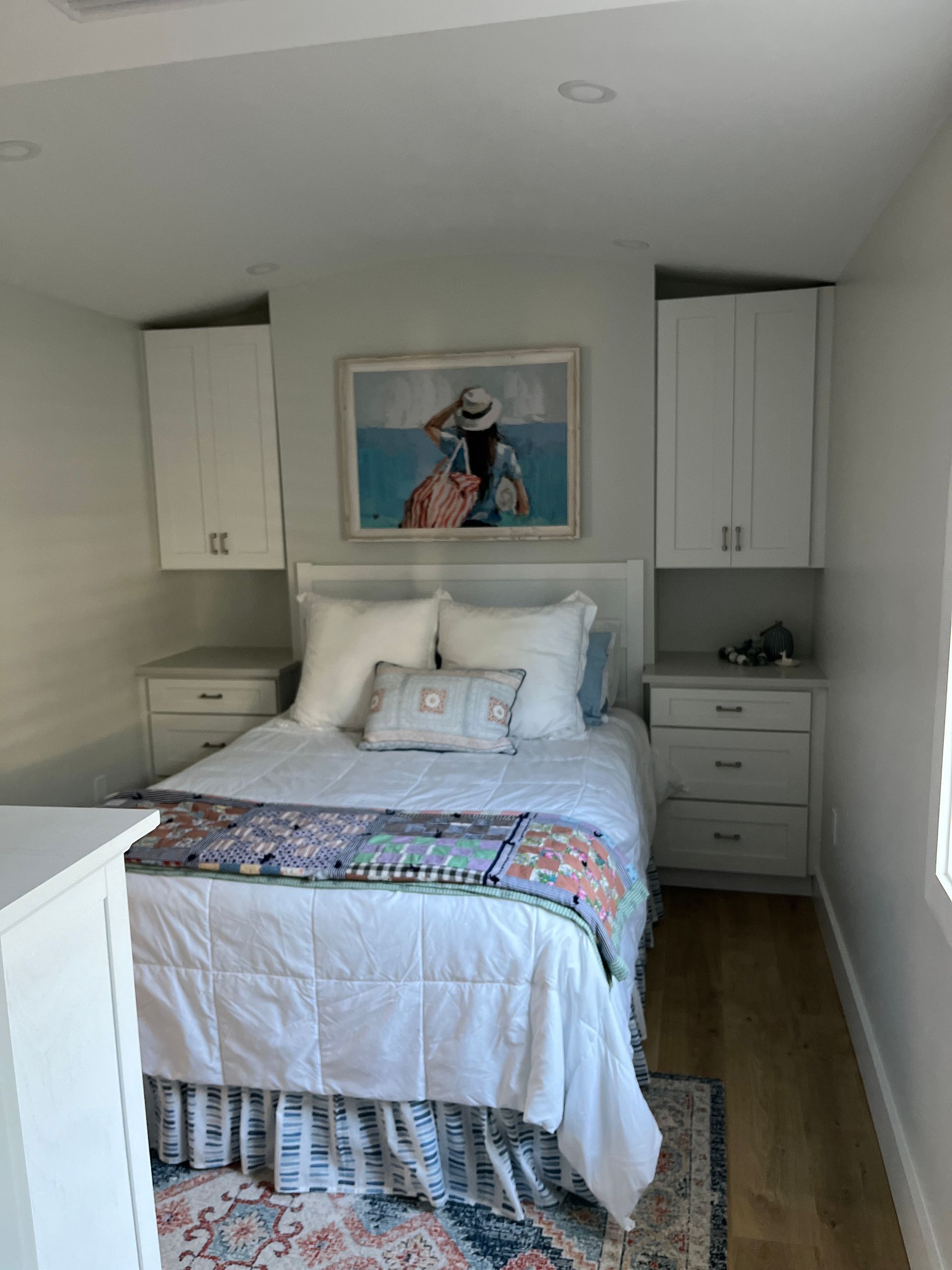 Bedroom with bed, nightstands, cabinets, art, and patterned bedding; light and airy space.