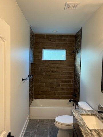 Bathroom with brown tiled shower, white tub, toilet, and vanity with gray counter.