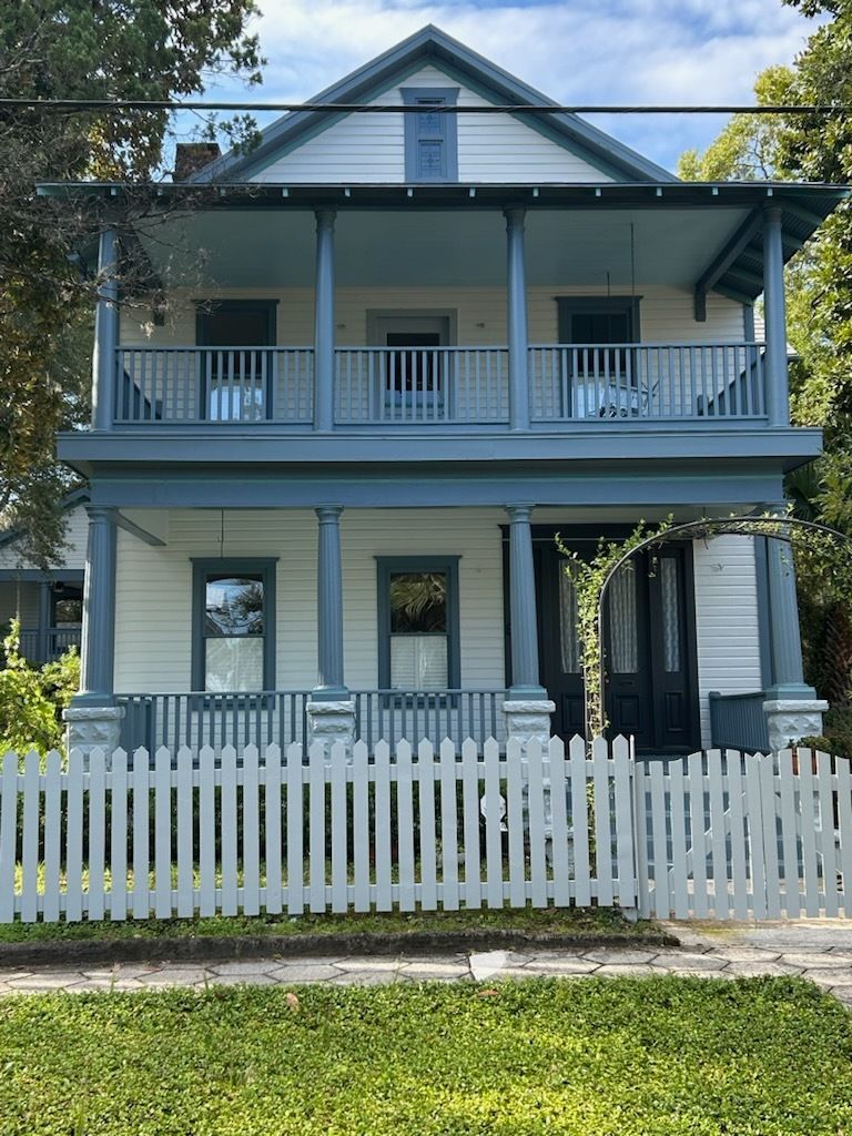 Two-story white house with blue trim, a porch, and a white picket fence.