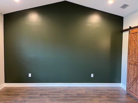 Empty room with a dark green accent wall, brown sliding door, and wood flooring.