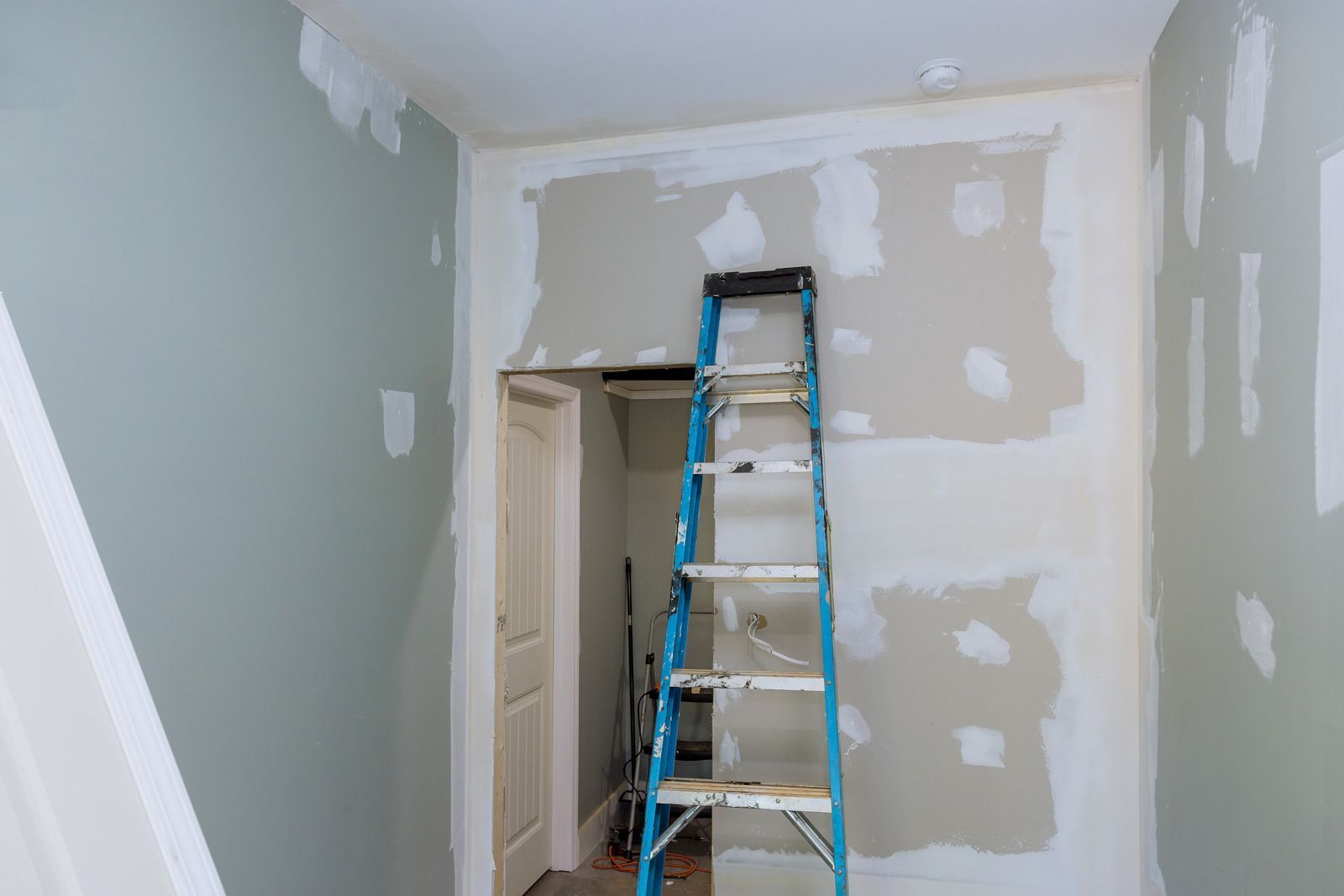 Interior room with walls partially painted and ladder propped against unfinished wall near doorway.