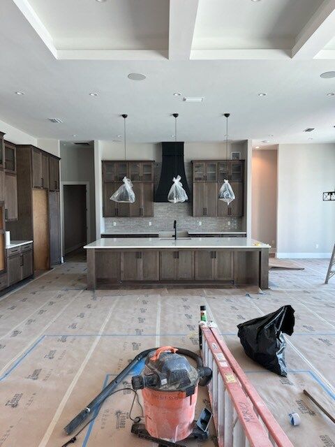 Kitchen under construction with island, cabinets, and hanging lights. Brown and gray tones dominate.