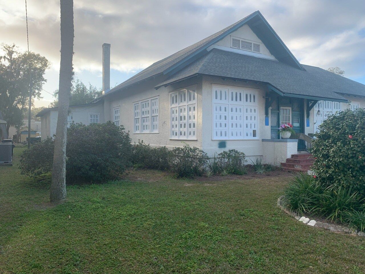 A white house with a gray roof is surrounded by grass and trees.