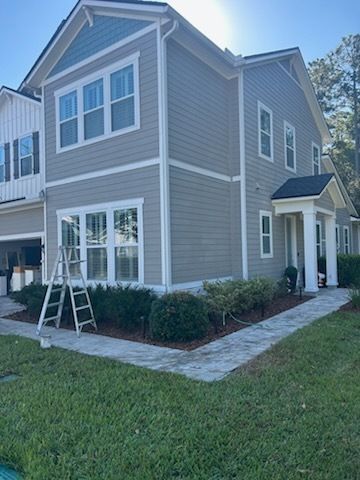 Two-story house with gray siding, blue accents, white trim, and a ladder, on a sunny day.