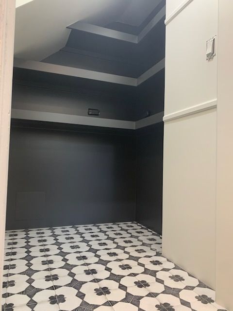 Empty room with black walls and ceiling. White and black patterned tile flooring. Bright, off-white wall to the right.