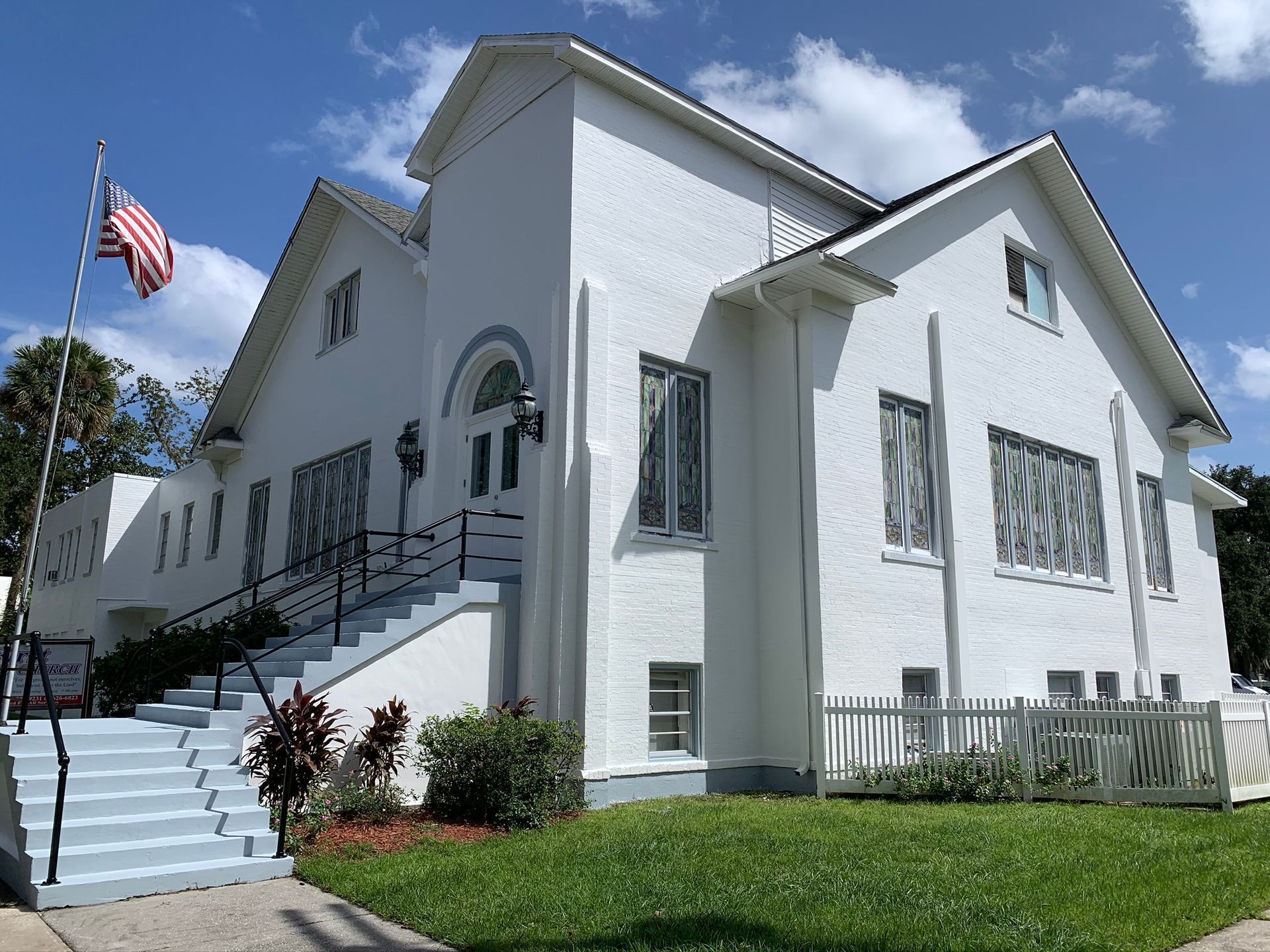 White church with stairs, arched windows, and American flag on a sunny day