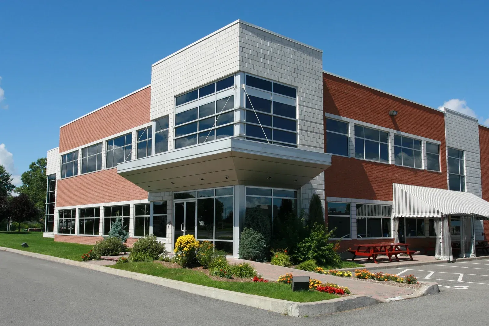Modern two-story brick and glass office building with landscaped entrance and striped awning