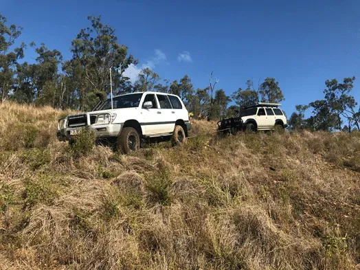 Two White Off-road Vehicles Parked on a Grassy Hillside Under a Blue Sky — Fitzroy Towing & Transport in Emerald, QLD