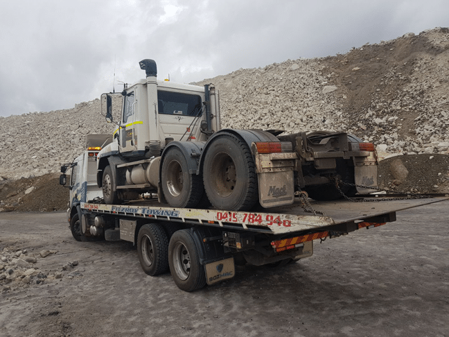 Truck on a Flatbed Tow Truck, on a Dirt Road With a Rocky Backdrop — Fitzroy Towing & Transport in Emerald, QLD