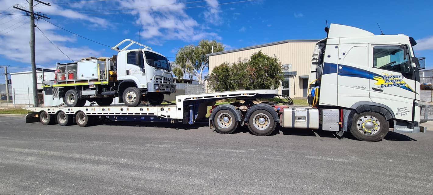 A Semi-truck With a Flatbed Trailer Carrying a Truck, Parked on a Paved Surface — Fitzroy Towing & Transport in Emerald, QLD