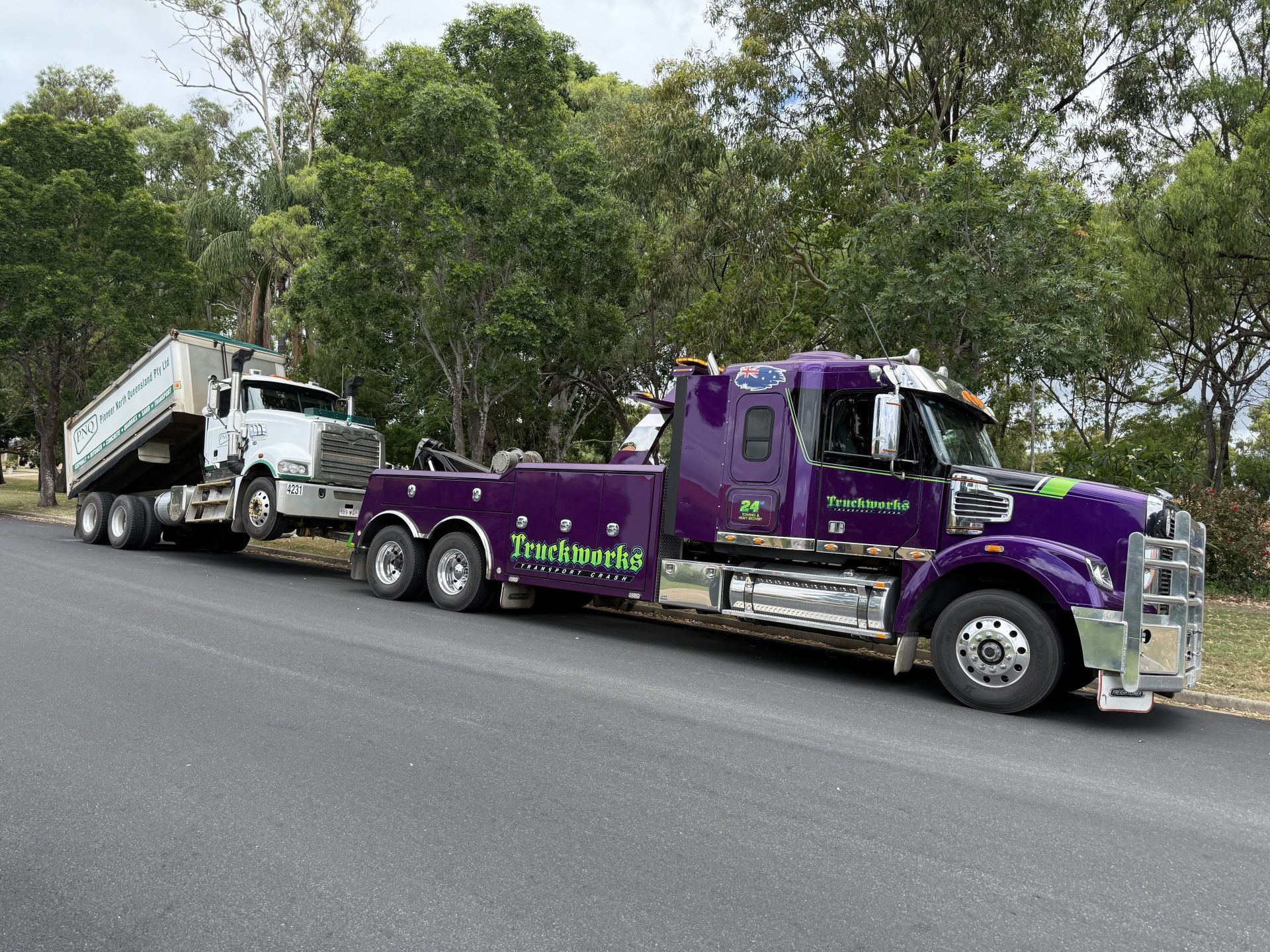 Purple tow truck towing a white dump truck on a road near trees.— Fitzroy Towing & Transport in Parkhurst, QLD