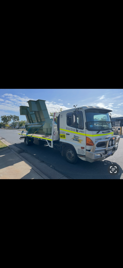 A white and yellow Hino truck carries a large green object on its flatbed in a parking lot.— Fitzroy Towing & Transport in Parkhurst, QLD