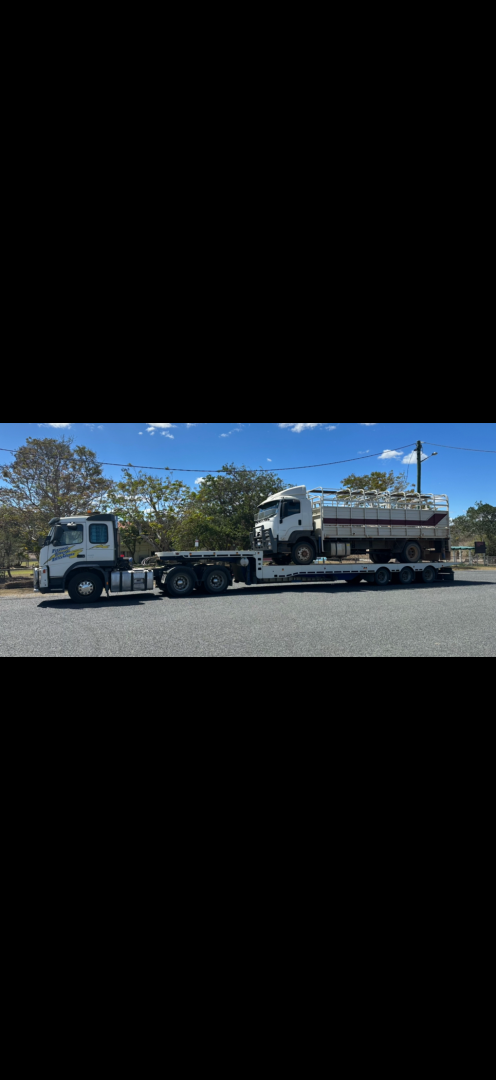 Two trucks, one towing a flatbed with another truck and tank on it, parked outdoors.— Fitzroy Towing & Transport in Parkhurst, QLD
